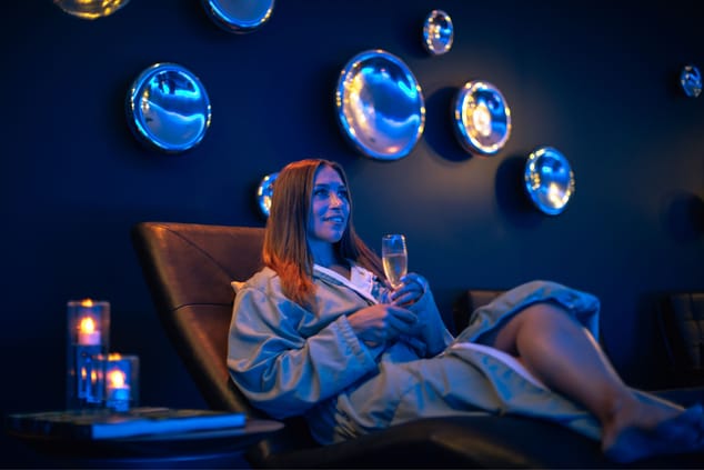 Woman enjoying champagne on chair in blue-lit room