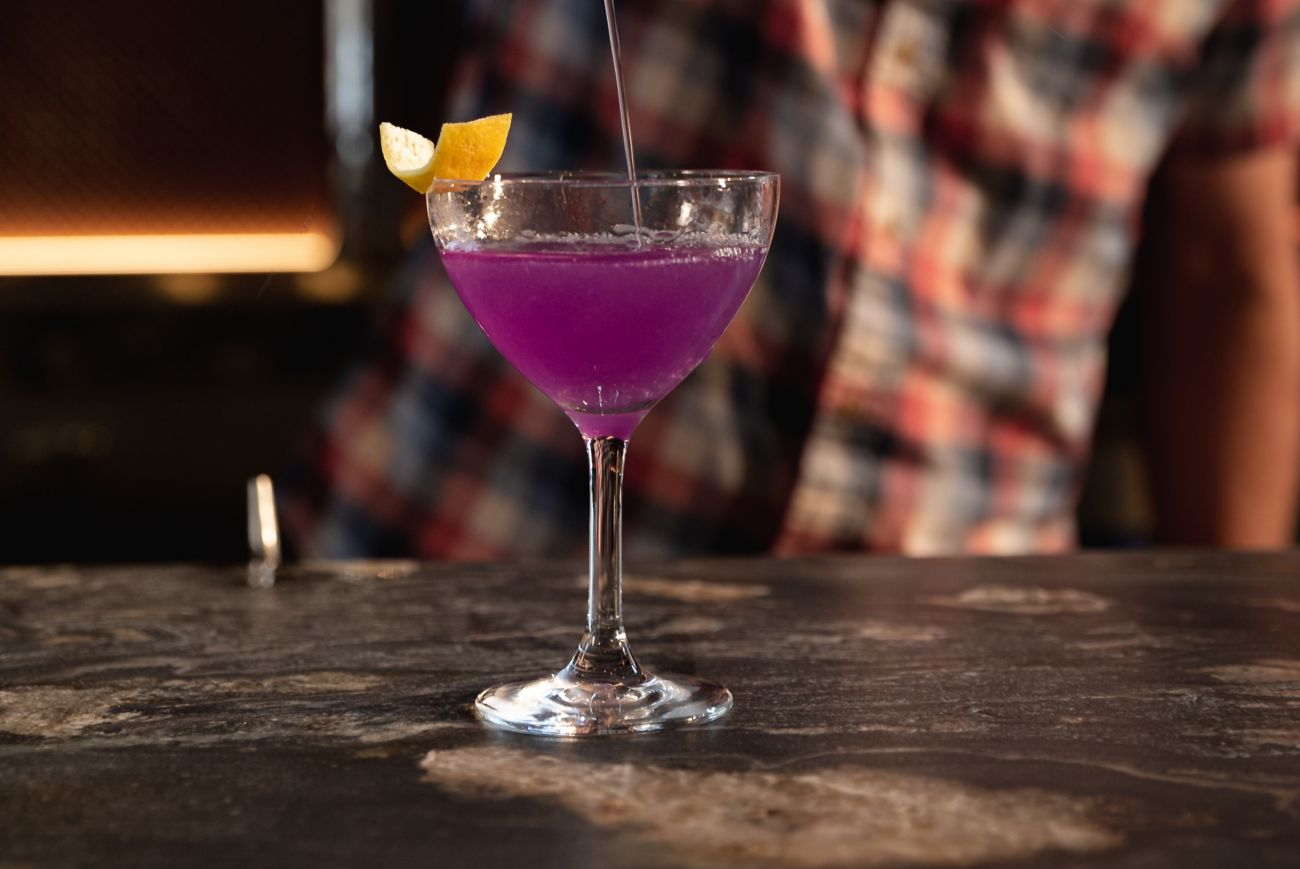 Bartender pouring a purple cocktail into a glass