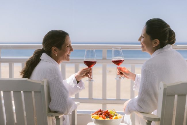 Two women drinking wine in robes on balcony