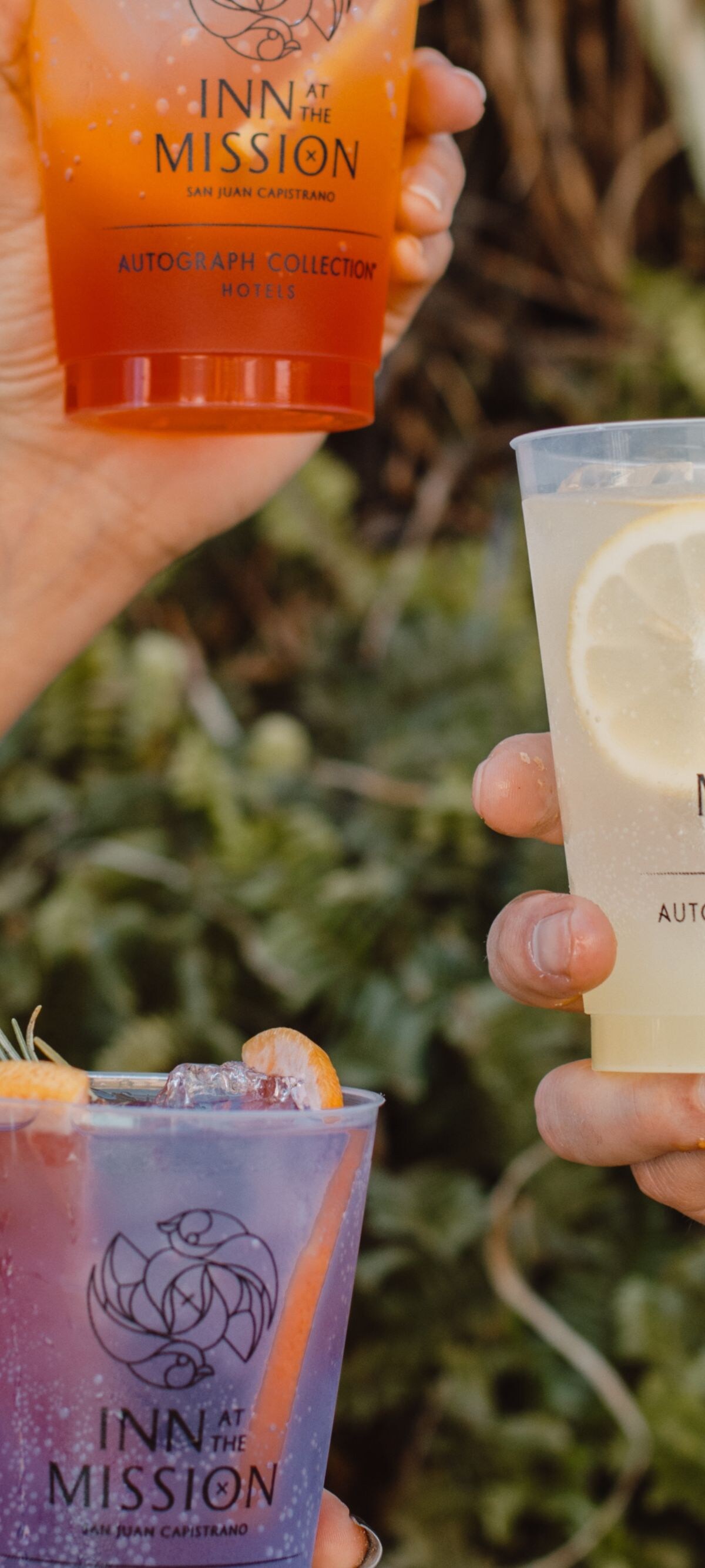 Three hands holding colorful cocktails in branded 