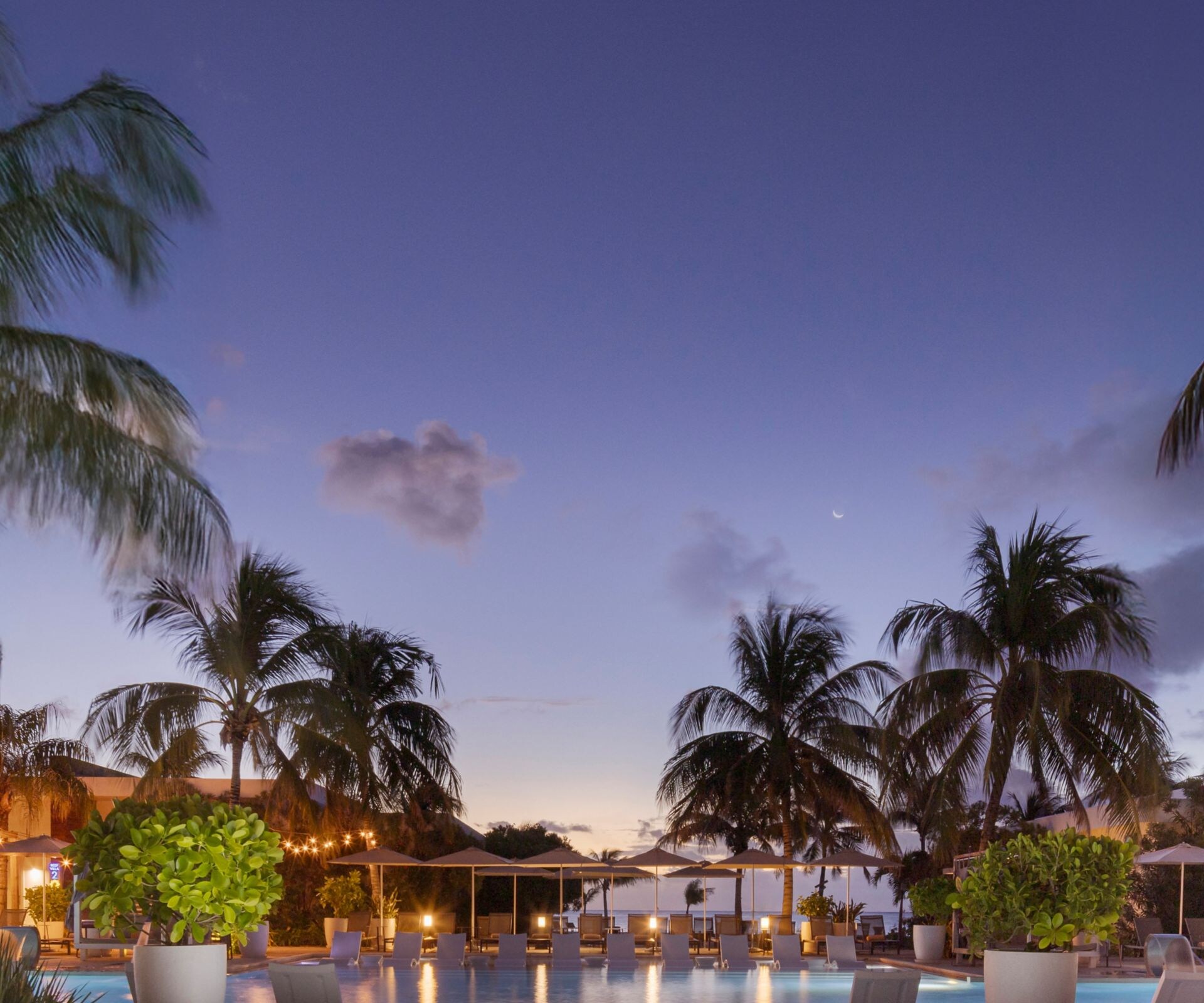 Resort pool at dusk with palms and cabanas