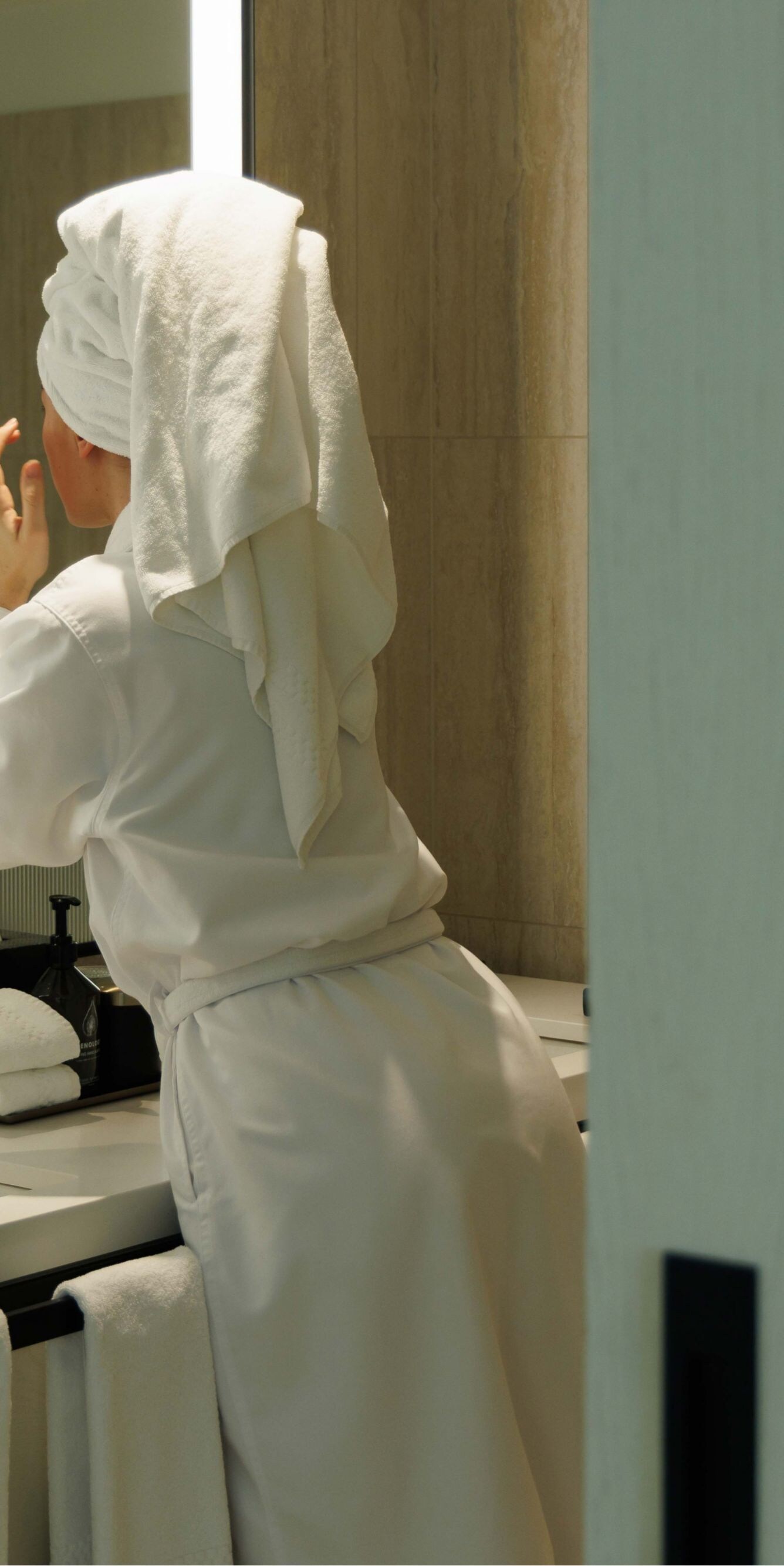 Client en peignoir se lavant le visage dans une salle de bain moderne