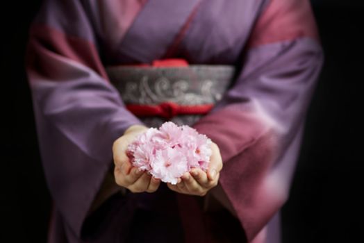 Woman wears a purple ombre kimono with her hands cupped in front of her holding pink blossoms