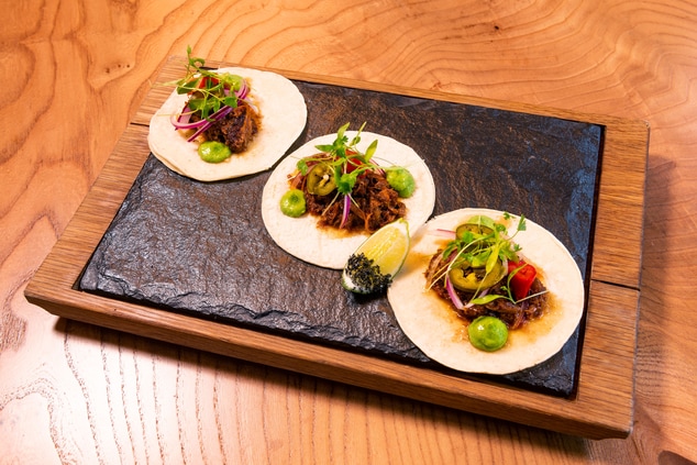 Three steak tacos with fixings on a black dish.