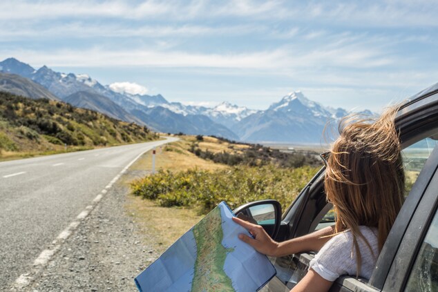Woman leaning out car window holding a map 