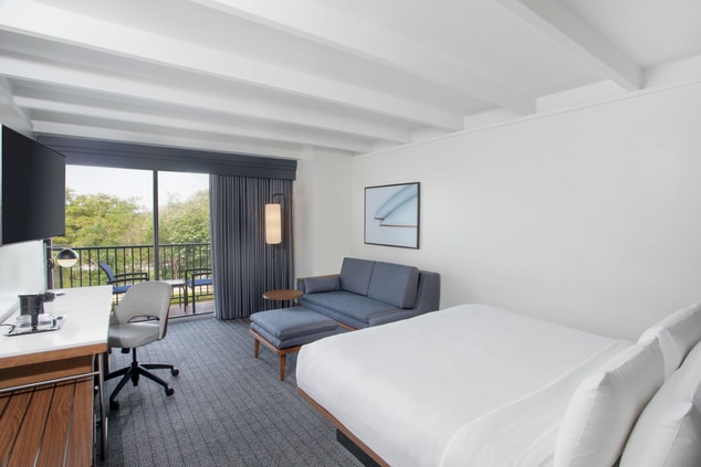 A hotel bed with a work desk and balcony.