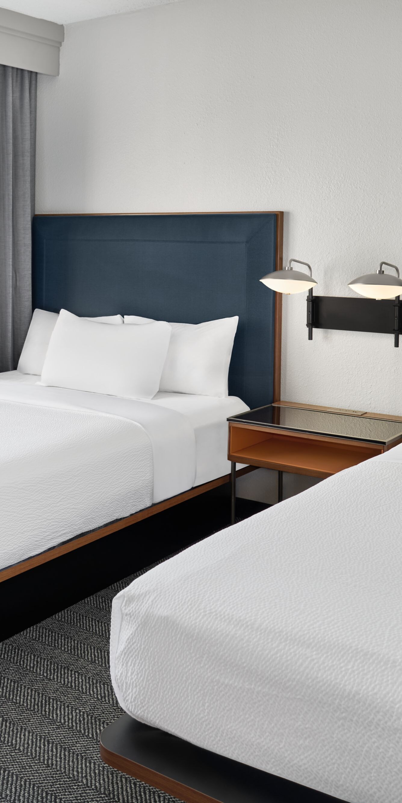 Two beds with blue headboards and window curtains