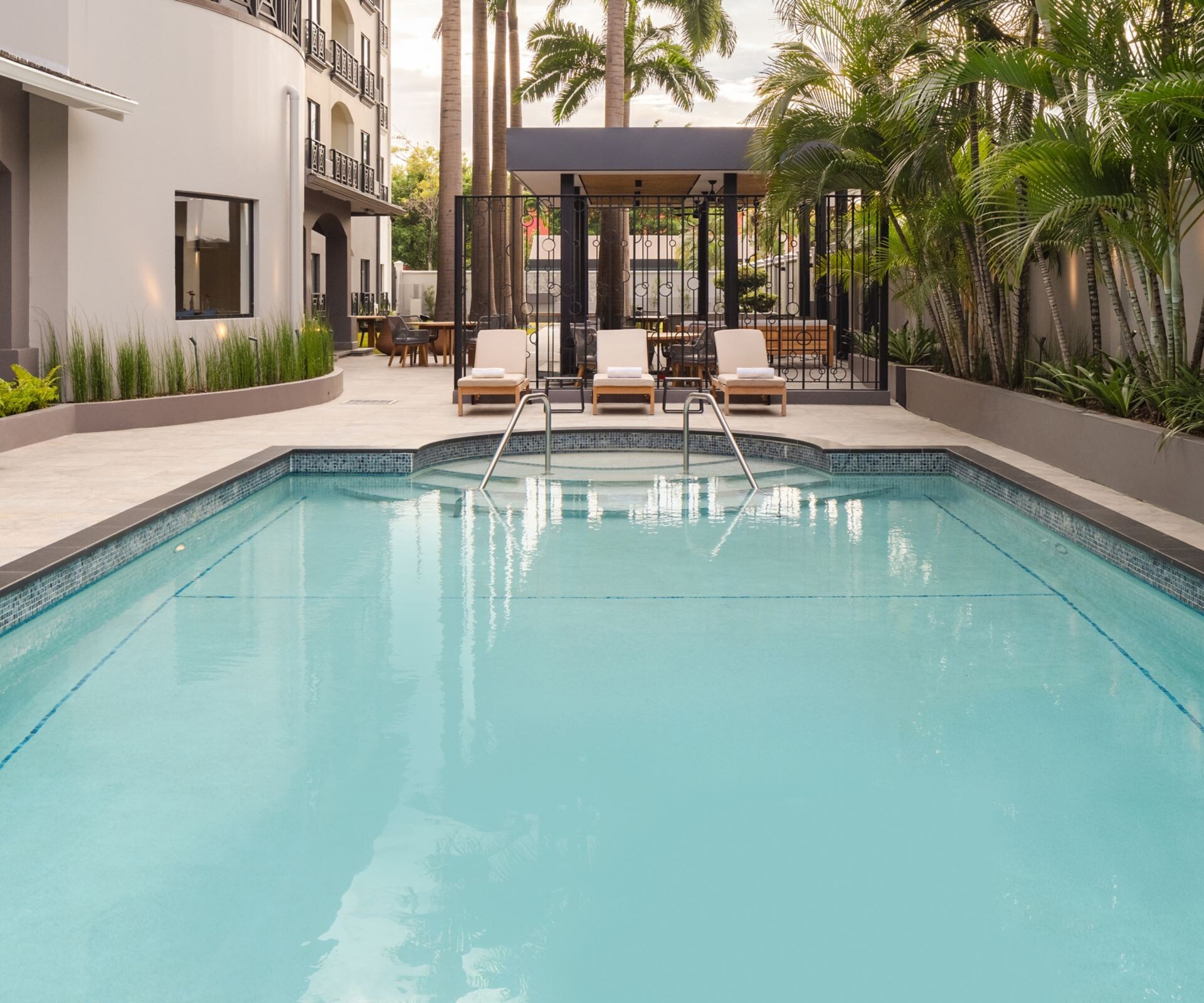 Piscina al aire libre con palmeras y edificio del hotel.