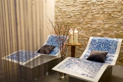 Two undulating blue lounge chairs in a quiet space with two candles and decorative branches