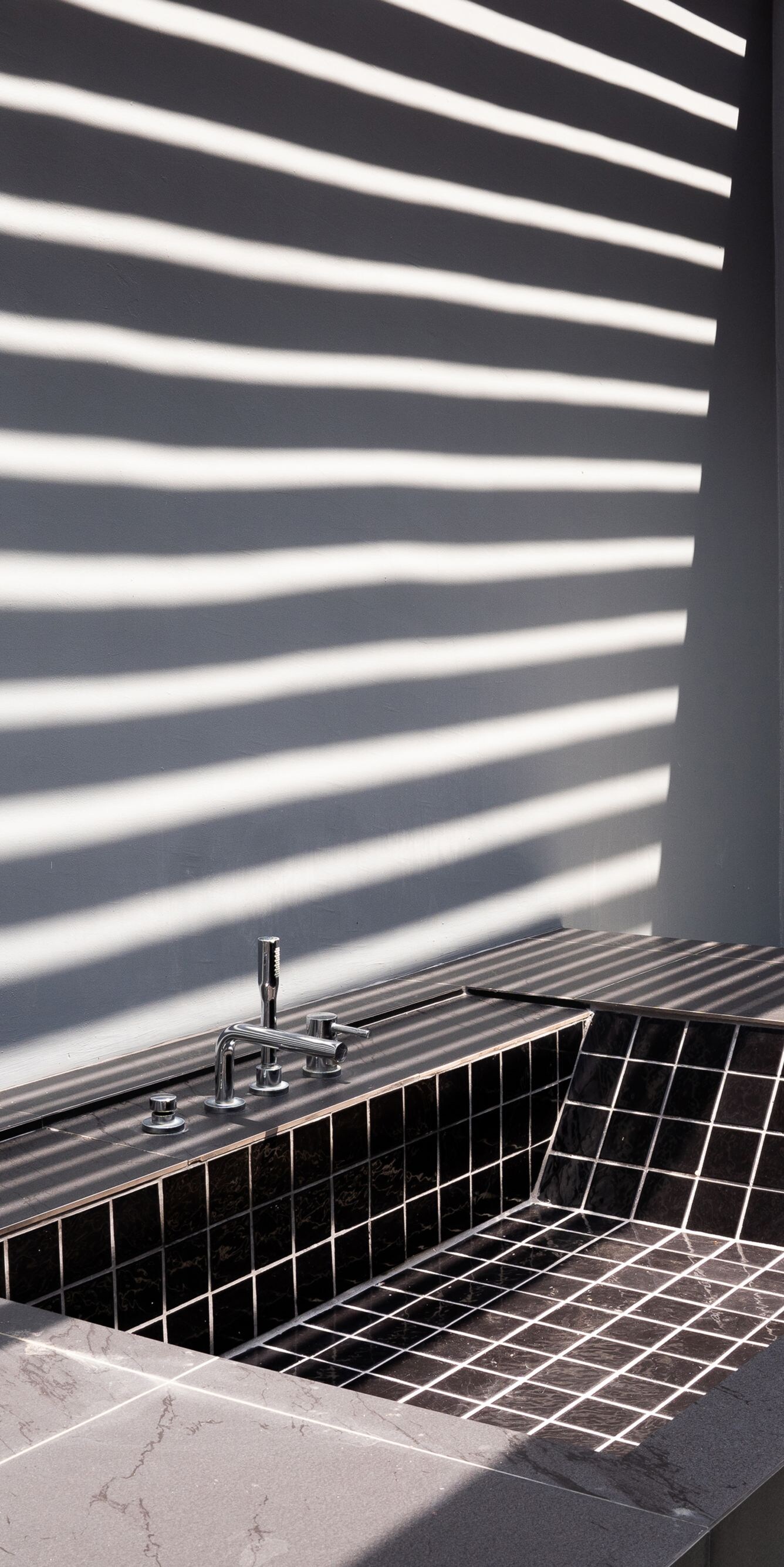 Black tiled soaking tub under striped light shadow