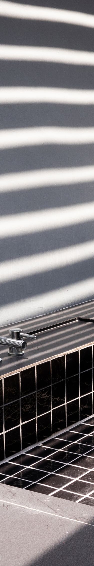 Black tiled soaking tub under striped light shadow