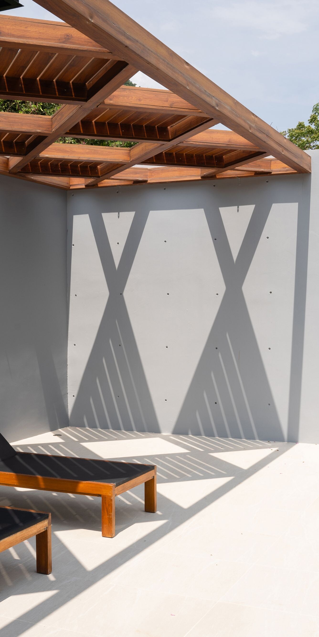 Two lounge chairs under wooden pergola by pool