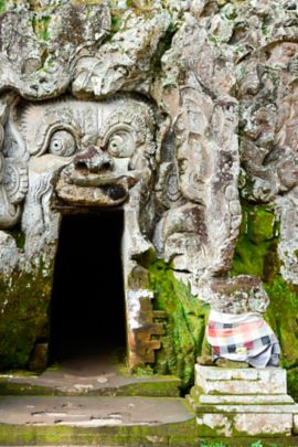 Exaggerated faces carved into the stone exterior of a cave around a small doorway