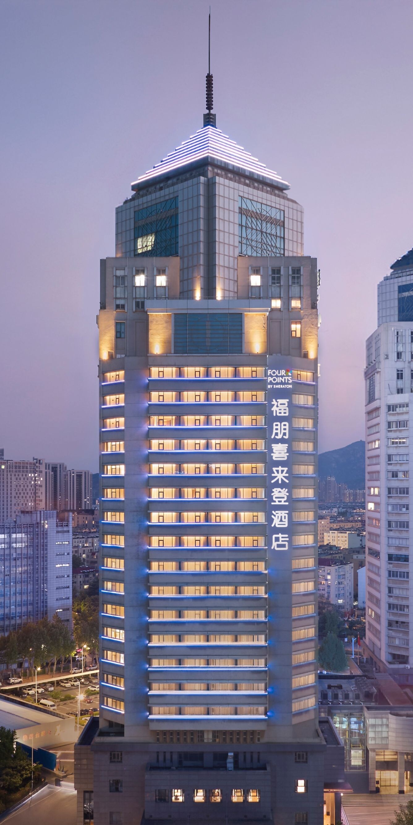 Tall glowing Four Points hotel tower against dusk 