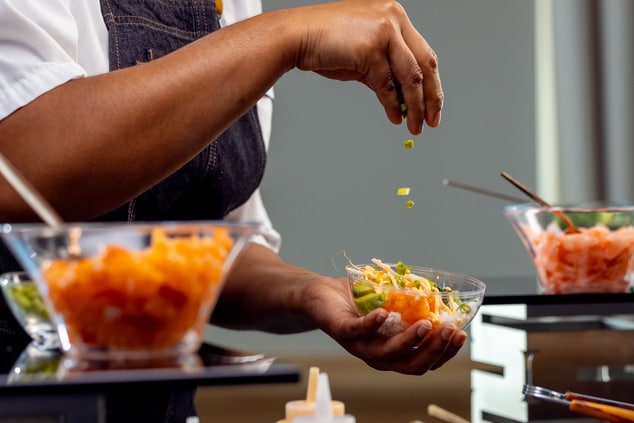 A chef sprinkling ingredients into a bowl