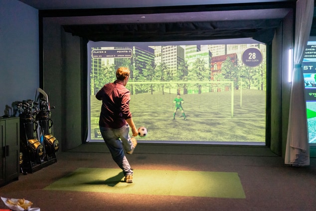 A man kicks a soccer ball at a virtual game screen