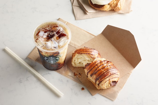 Iced coffee next to a torn chocolate croissant