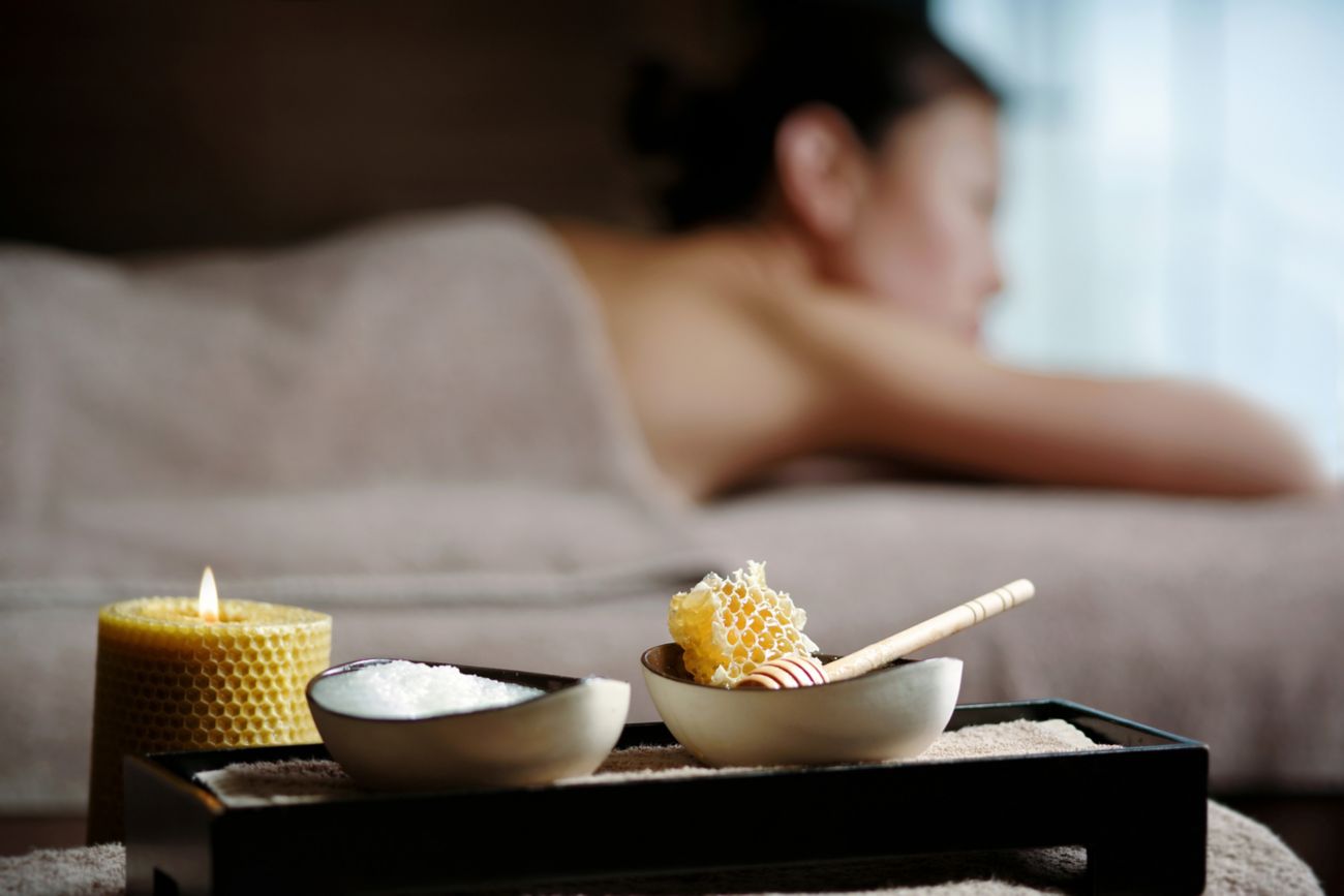 A bowl of white cream and a bowl of honeycomb sit on a tray with a woman lying down in the background