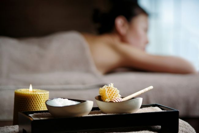 A bowl of white cream and a bowl of honeycomb sit on a tray with a woman lying down in the background