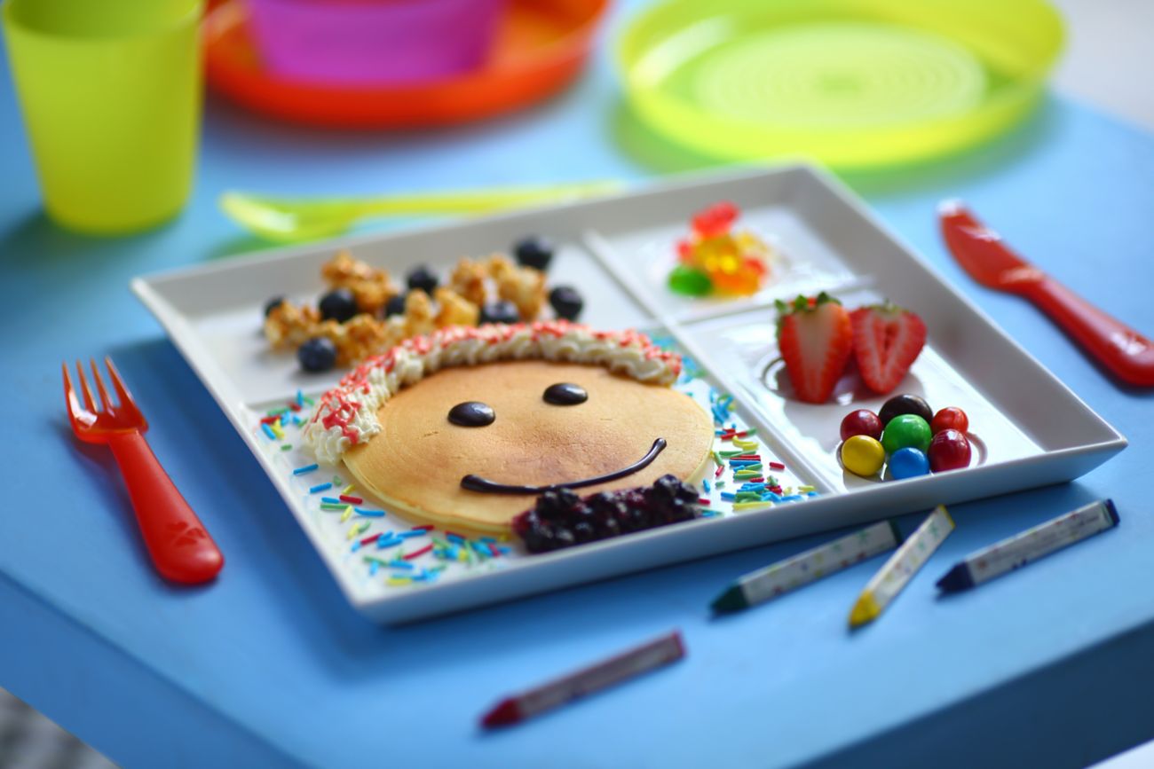 A sectioned plate with a smiley face pancake, gummy candies and strawberries