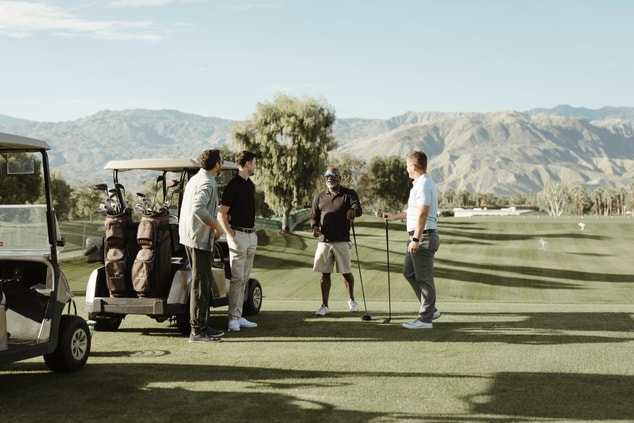 Four people standing around golf carts on course