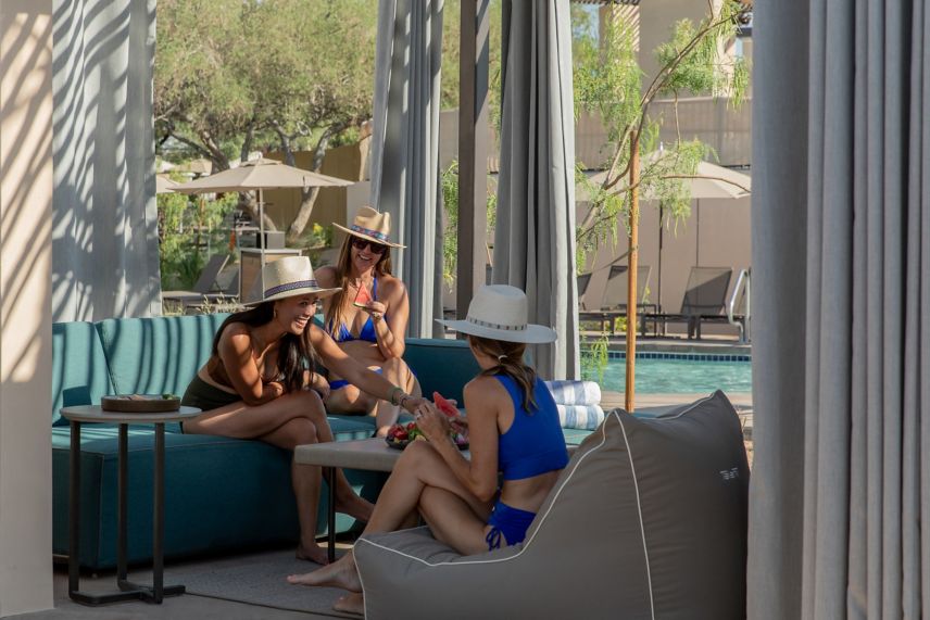 Three women eating fruit in a poolside cabana