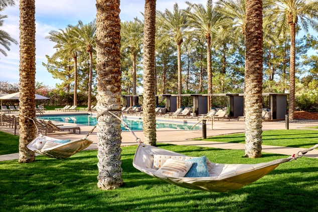 Two hammocks between palm trees with pool in back
