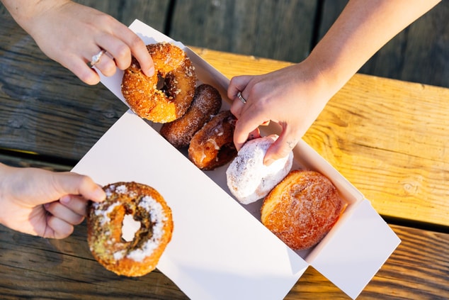 hands reaching into box with assorted doughnuts