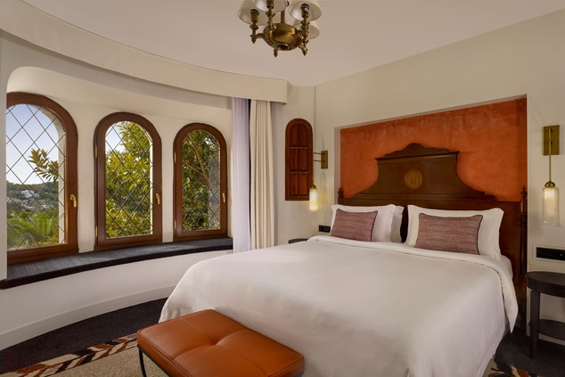 Bed with three windows overlooking lush greenery.