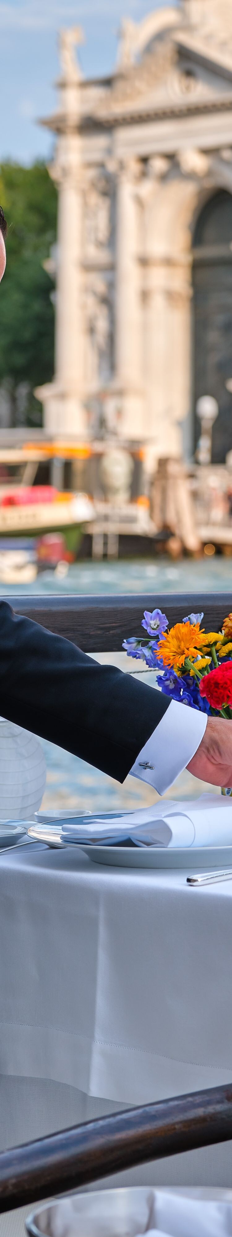 Ein Kellner, der den Esstisch mit Gläsern im Freien deckt.