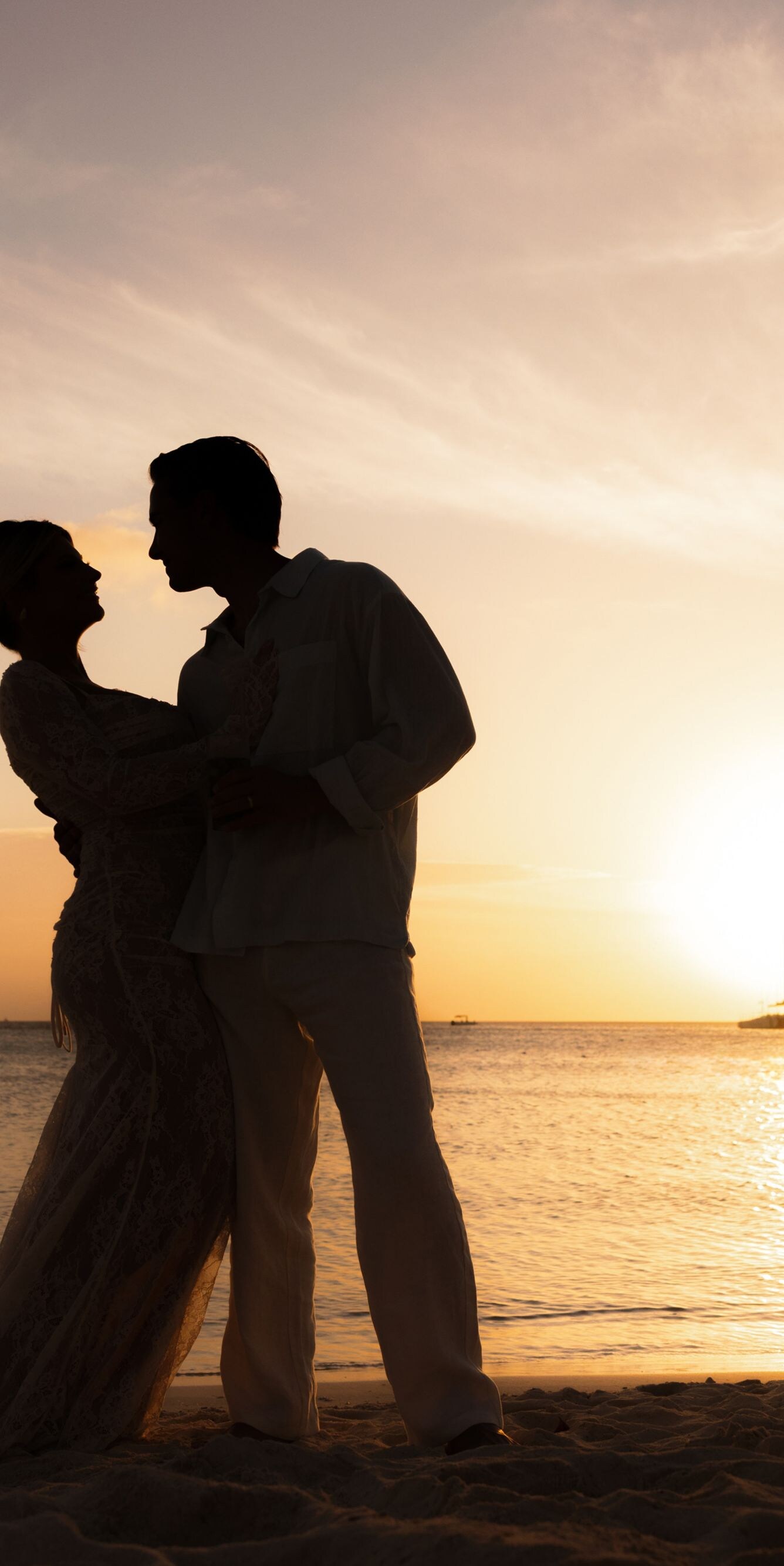 Two people standing on a sandy beach at sunset