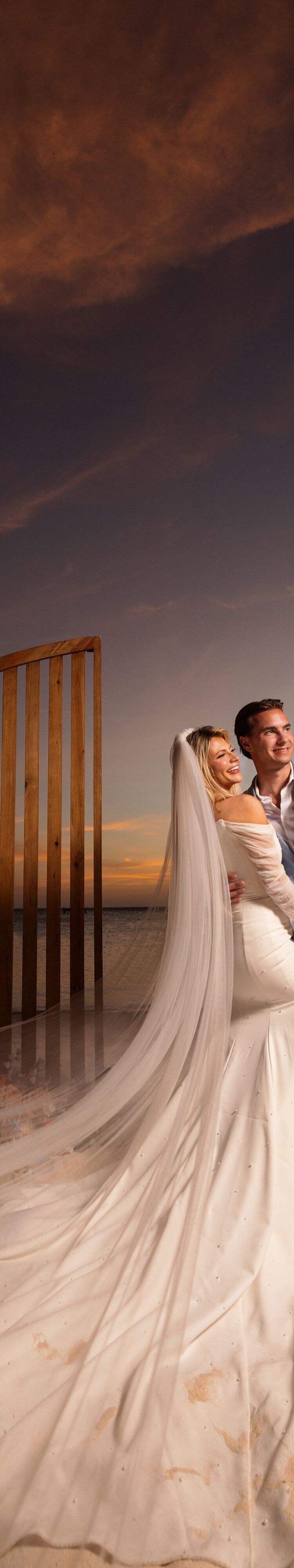 Beach wedding couple by floral arch at sunset
