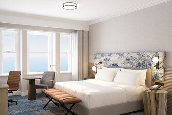 A foto mostra uma cama, cadeira e vista para o mar