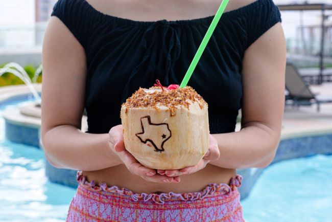 Model holding a pina colada in a coconut cup.