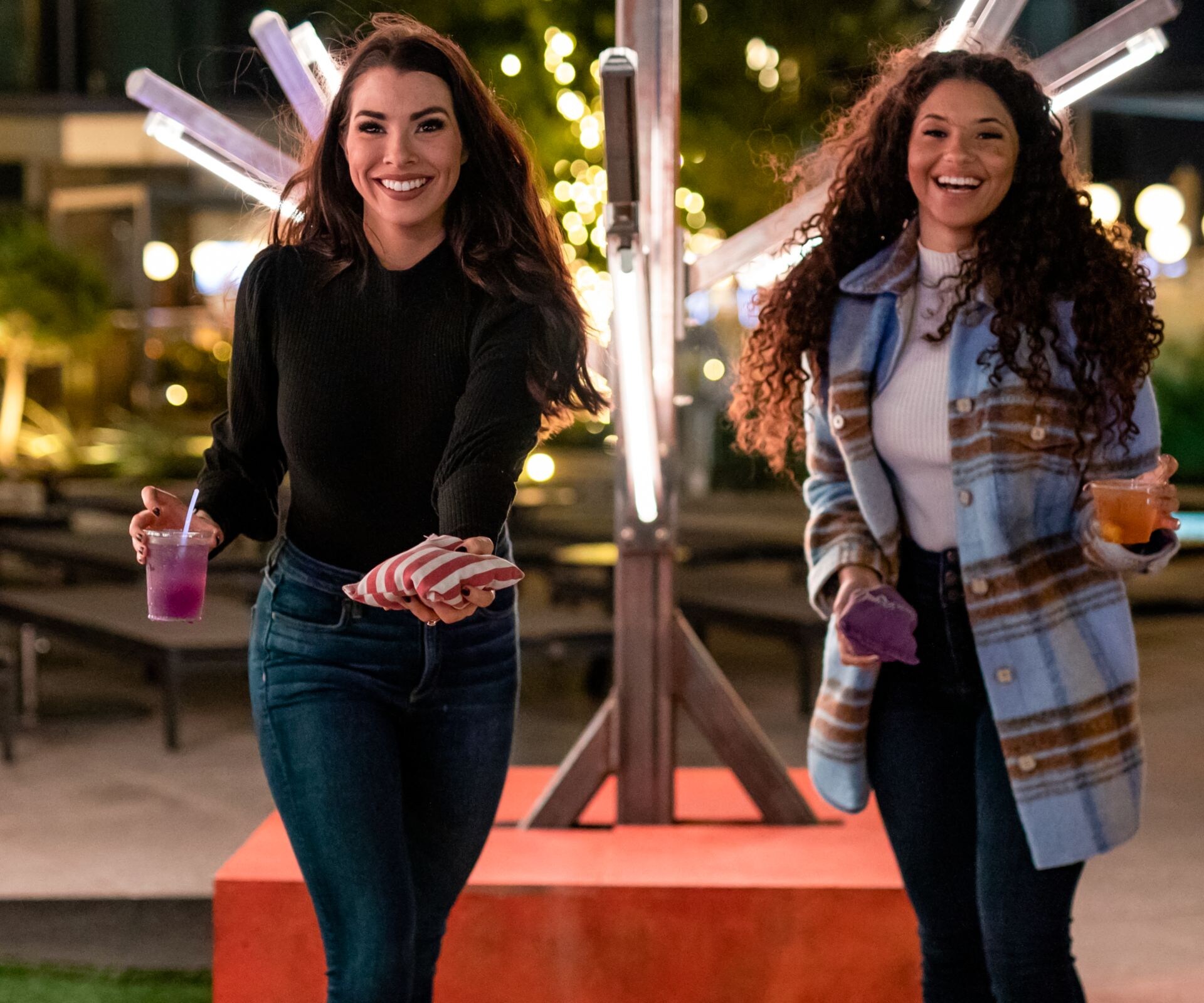dos mujeres jugando cornhole y tomando cócteles