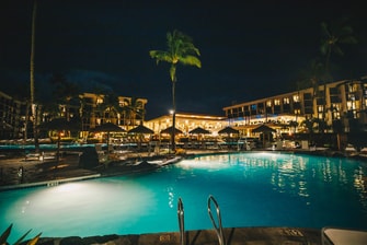 Pool lit up at night with hotel in background.