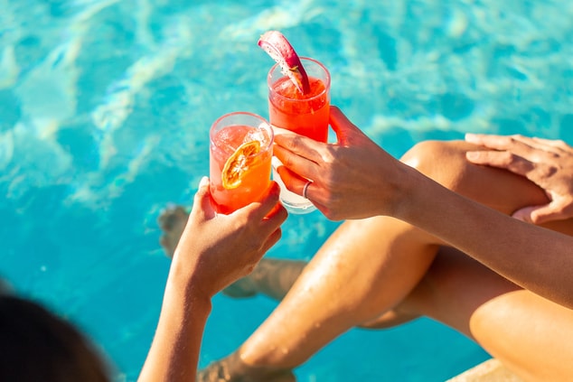Two female hands holding fruit cocktails at pool