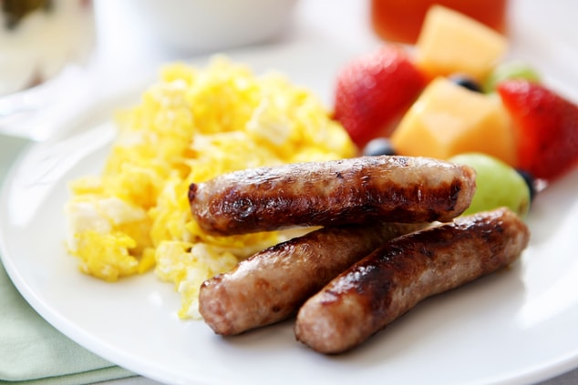 Photo of a plate full of eggs, sausage, and fruit
