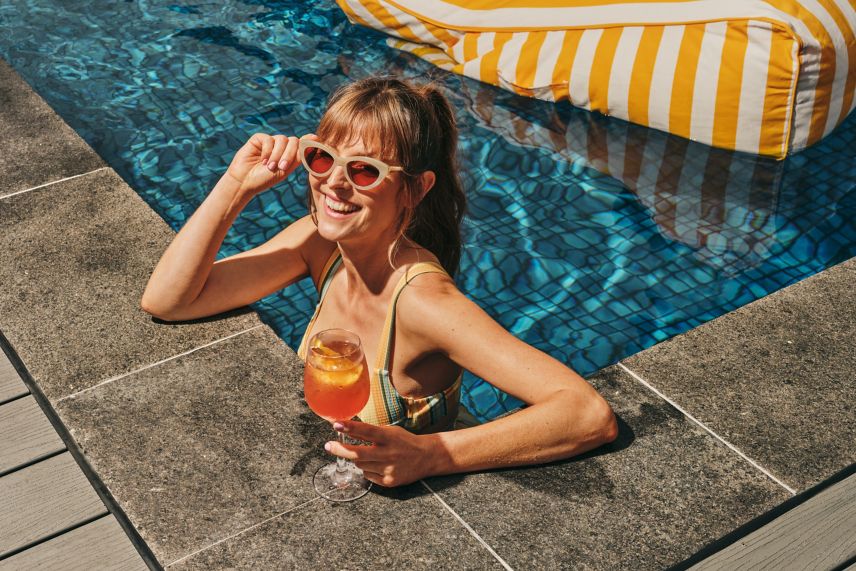 Woman wearing sunglasses in a pool with a cocktail