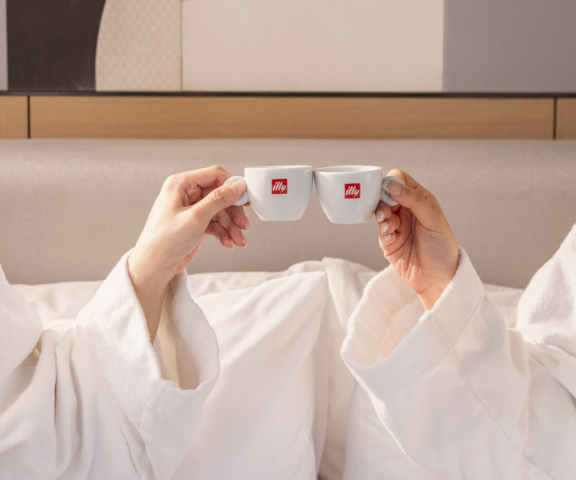 Two women relax in bed with illy coffee.