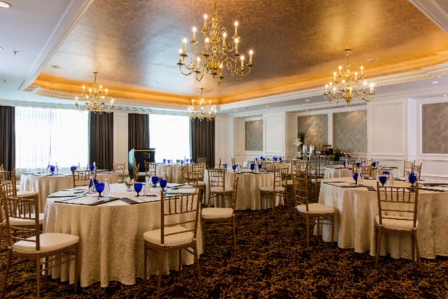 Function room with a recessed ceiling, natural light, soffit and chandelier lighting, white wall paneling and roundtables