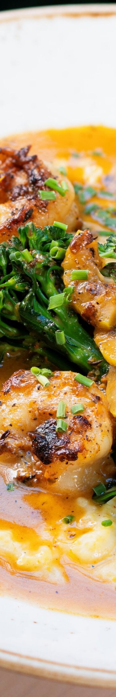 Shrimp, broccolini, grits in a white bowl.
