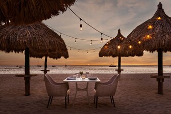 Mesas y sillas dispuestas para la cena en la playa al atardecer
