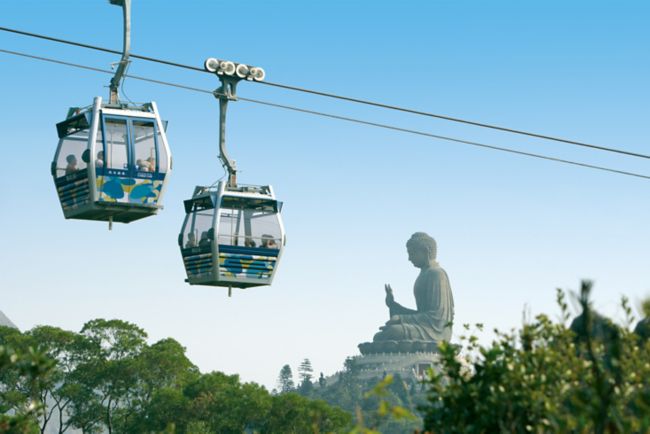 Two cable cars cross while a large Buddha statue sits in the background
