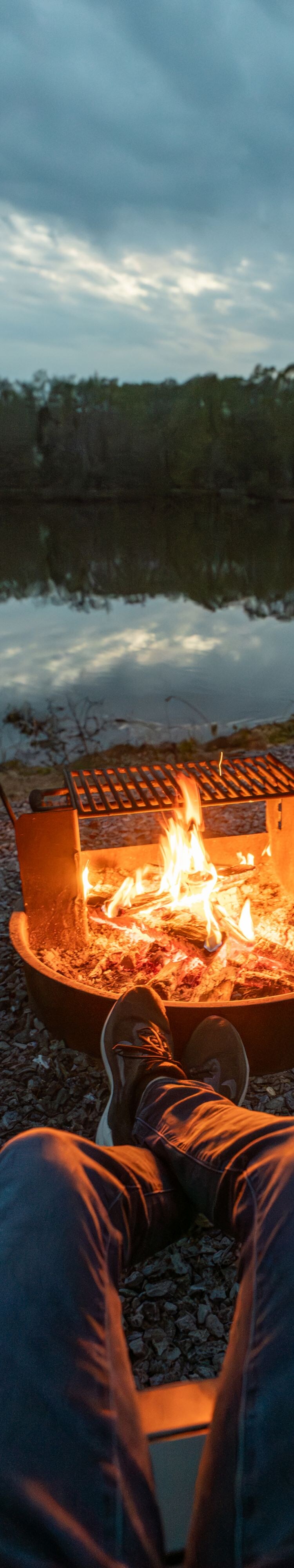 person sitting fire pit next to a lake 