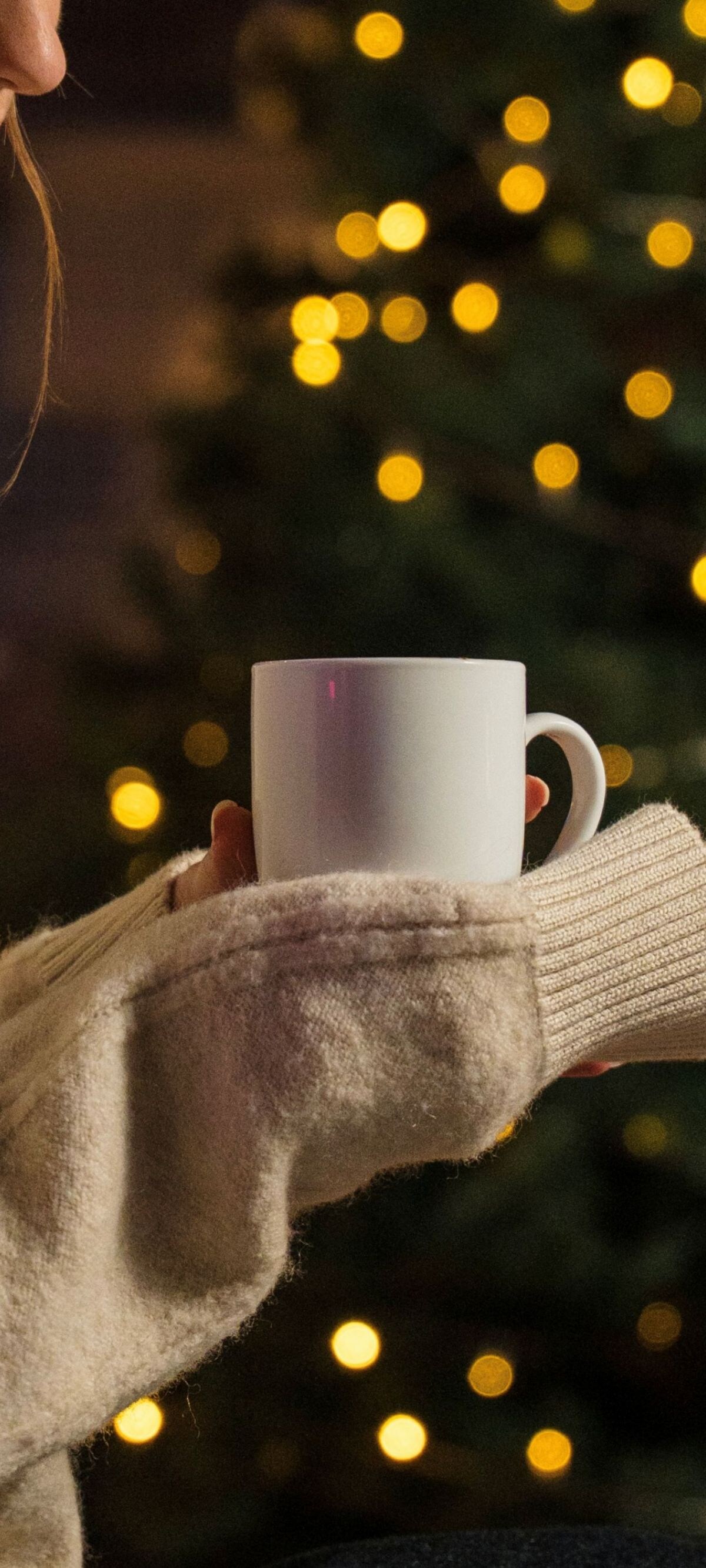 Woman holding a mug beside a lit Christmas tree