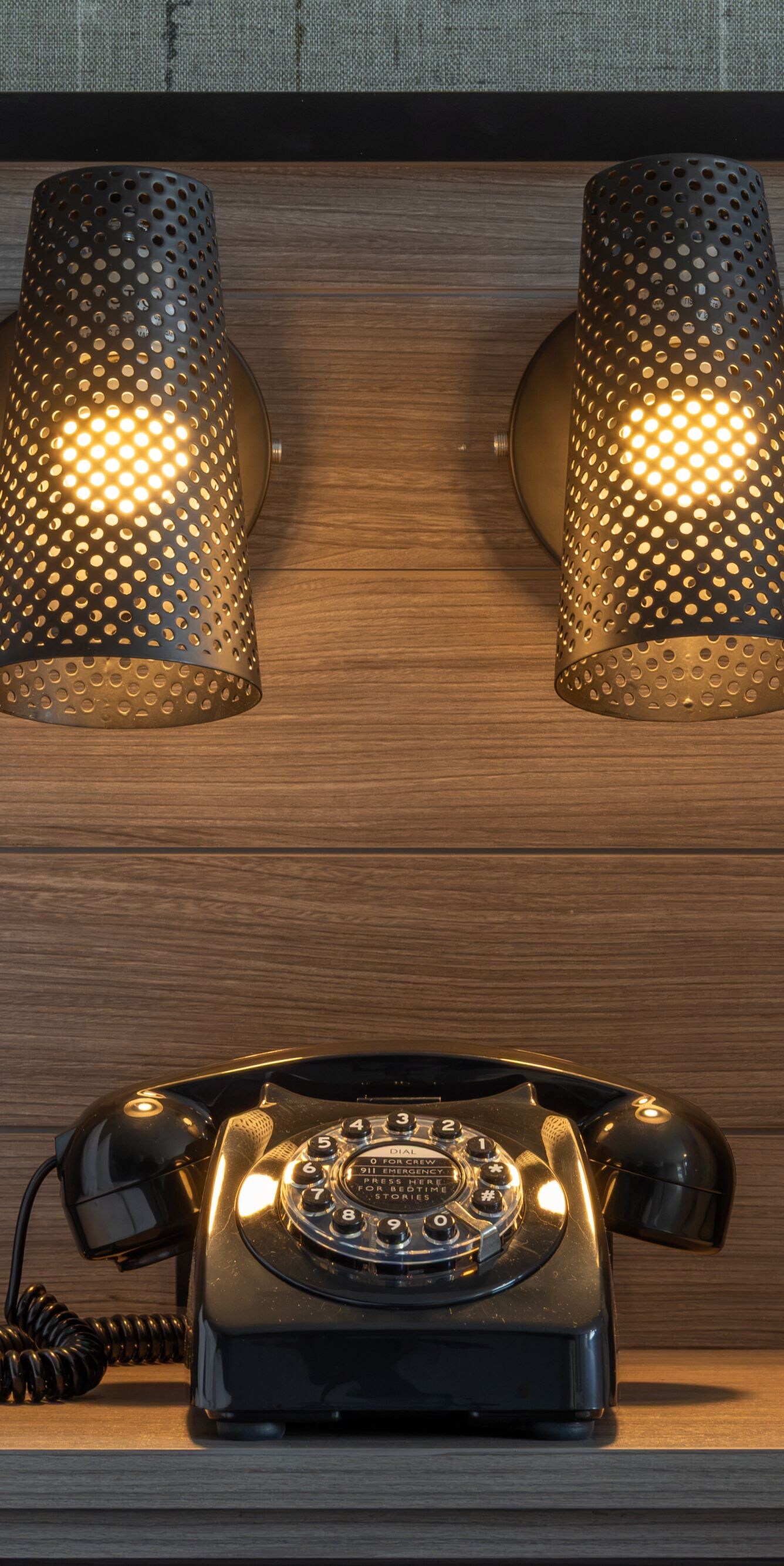 A rotary style phone on a night stand with lights.