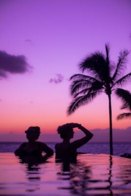 Two woman in an infinity pool during sunset.