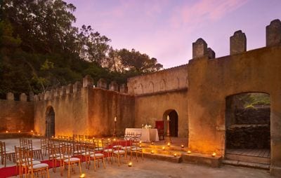 An open-air courtyard framed by stone walls with rows of chairs set for a wedding ceremony