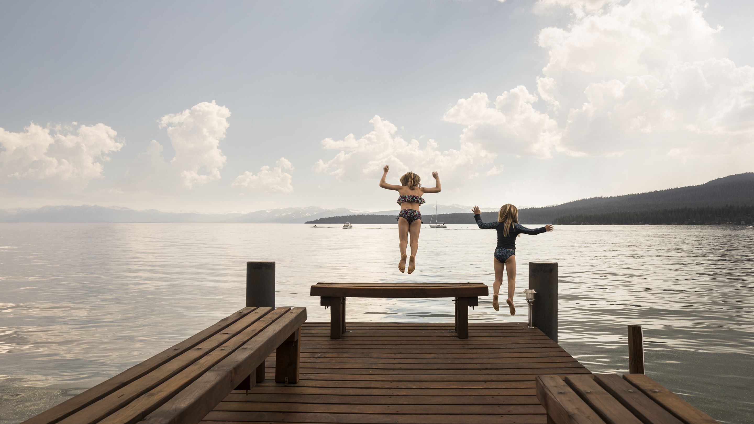 Two girls jump off a pier into a lake